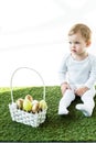 Kid sitting near straw basket with colorful Easter eggs isolated on white Royalty Free Stock Photo