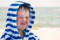 A cute kid in a terry dressing gown with atopic dermatitis, squinting. A child with dry red skin on his face, an allergy