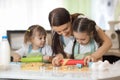 Cute little kids and their beautiful mom in aprons are playing and laughing while kneading the dough in the kitchen Royalty Free Stock Photo