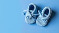 Cute knitted baby booties on blue background with copy space