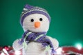 Cute knitted white snowman with a carrot for a nose and a striped hat on a green background, horizontal Christmas banner. New year