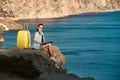 Cute lady work sitting on rock. Bright yellow luggage for trip. Remote office and business travel concept, copy space