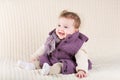 Cute laughing baby girl in purple jacket on knitted