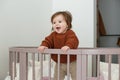 Cute laughing baby standing in round bed. Little girl learns to stand in her crib Royalty Free Stock Photo