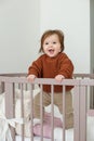 Cute laughing baby standing in round bed. Little girl learns to stand in her crib Royalty Free Stock Photo