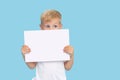 A cute laughing child boy is holding a white signboard with an empty space for text. Advertising of childrens