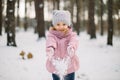 Cute laughing child girl having fun in winter forest. Little girl in pink coat throwing the snow and smiling. Seasonal Royalty Free Stock Photo