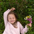 A cute laughing little girl, laying on the grass and taking a bouquet of field flow Royalty Free Stock Photo