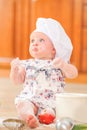 Cute liitle girl in chef`s hat sitting on the kitchen floor soil