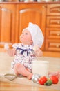 Cute liitle girl in chef`s hat sitting on the kitchen floor soil