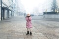 Cute liitle sad lost caucasian girl in warm long pink jacket and hat feel horror on empty street of old european city Royalty Free Stock Photo