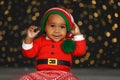 Cute Little African American Baby Wearing Elf Hat Against Blurred Lights On Dark Background. Christmas Celebration