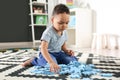 Cute little African-American child playing with puzzles on floor in kindergarten