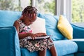 Cute little african american girl sitting on the sofa and playing on tablet in the living room Royalty Free Stock Photo