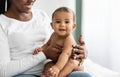 Cute little African American infant sitting on bed with mother Royalty Free Stock Photo