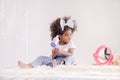 The cute little African girl happily uses an electric hair dryer in her bedroom