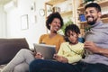 Little Afro-American girl and her beautiful young parents using digital tablet and doing shopping online while sitting on a Royalty Free Stock Photo