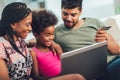 Little Afro-American girl and her beautiful young parents using a laptop and doing shopping online while sitting on a sofa at Royalty Free Stock Photo