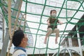 Cute little Asian boy child wearing washable face mask climb on jungle gym at pulbic indoor playground with his father during Royalty Free Stock Photo