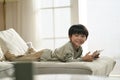 cute little asian boy lying on front on couch with digital tablet Royalty Free Stock Photo