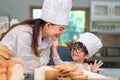 Cute little Asian boy painting beautiful woman face with dough flour. Chef team playing and baking bakery in kitchen funny. Royalty Free Stock Photo