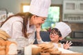 Cute little Asian boy painting beautiful woman face with dough flour. Chef team playing and baking bakery in home kitchen funny.