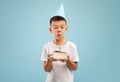 Cute Little Asian Boy In Party Hat Blowing Candle On Birthday Cake Royalty Free Stock Photo