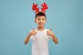 Cute Little Asian Boy Wearing Reindeer Horns Gesturing Thumbs Up At Camera Royalty Free Stock Photo