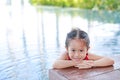 Cute little Asian child girl in a mermaid suit has fun sitting poolside