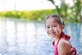 Cute little Asian child girl in a mermaid suit has fun sitting poolside