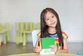 Cute little Asian child girl is playing with educational colors flashcards while sitting at table in children room