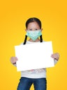 Cute little asian child girl wearing a protective mask with showing blank white paper isolated on yellow background. Kid holding Royalty Free Stock Photo