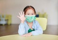 Cute little Asian child girl wearing a protective mask with showing five fingers sitting on kid chair in children room Royalty Free Stock Photo