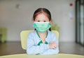 Cute little Asian child girl wearing a protective mask sitting on kid chair in children room Royalty Free Stock Photo