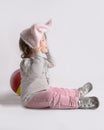 Beautiful playful mixed race asian baby girl in pink knitted hat sitting on a white background