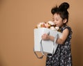 Cute little asian girl in beautiful spring dress holds a big basket of big white flowers pion and smells it