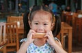 Cute little asian girl bite bread sheet. Asian girl having breakfast. Child looking at camera Royalty Free Stock Photo