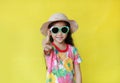 Cute little asian girl in floral summer dress wear hat and sunglasses isolated on yellow background pointing at camera. Holiday Royalty Free Stock Photo