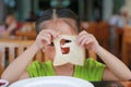 Cute little asian girl looking through hole of bite bread sheet. Asian girl having breakfast. Child looking at camera Royalty Free Stock Photo