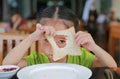 Cute little asian girl looking through hole of bite bread sheet. Asian girl having breakfast. Child looking at camera Royalty Free Stock Photo