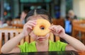 Cute little asian girl looking through hole of Donut. Asian girl having breakfast. Child looking at camera Royalty Free Stock Photo