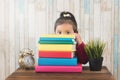 Cute little asian girl peeping from behind stack of books