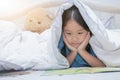 Cute little asian girl reading fairy tales book under blanket on Royalty Free Stock Photo