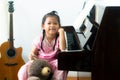 Cute little asian girl in traditional chinese dress sitting beside piano with her lovely teddy bear doll. Royalty Free Stock Photo