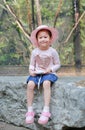 Cute little Asian girl wearing pink straw hat sitting on the stone against green public garden. Child girl looking at camera Royalty Free Stock Photo