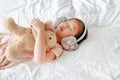 Cute little Asian girl wearing winter ear muffs and embracing teddy bear lying on the bed at home Royalty Free Stock Photo