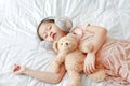 Cute little Asian girl wearing winter ear muffs with teddy bear lying on the bed at home Royalty Free Stock Photo