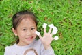 Cute little Asian kid girl lying on green grass lawn with showing empty white stickers on her fingers Royalty Free Stock Photo