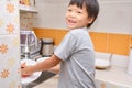 Cute little Asian kindergarten boy child doing the dishes, washing dishes in kitchen at home