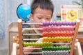 Cute little asian kindergarten 4 years old boy sitting on floor using the abacus with beads to learn how to count indoor at home
